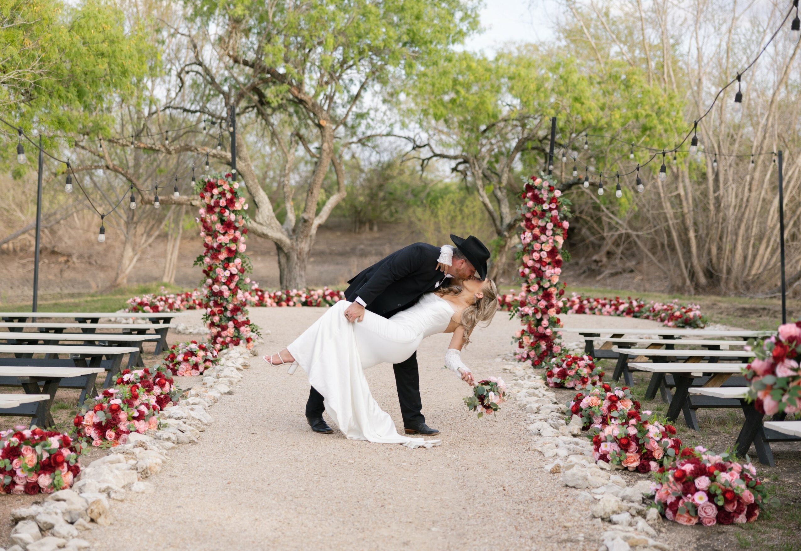 Couple dancing outdoors on a decorated pathway with floral arrangements and trees in the background.