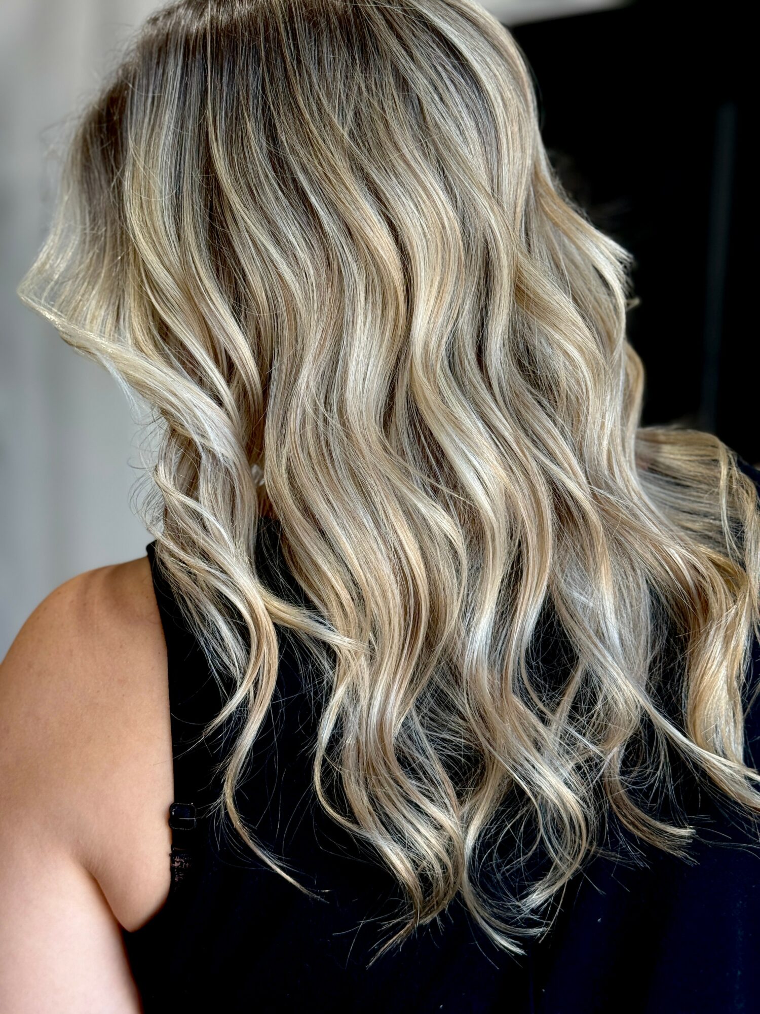 Wavy blonde hair with highlights on a person wearing a black top, viewed from the back.