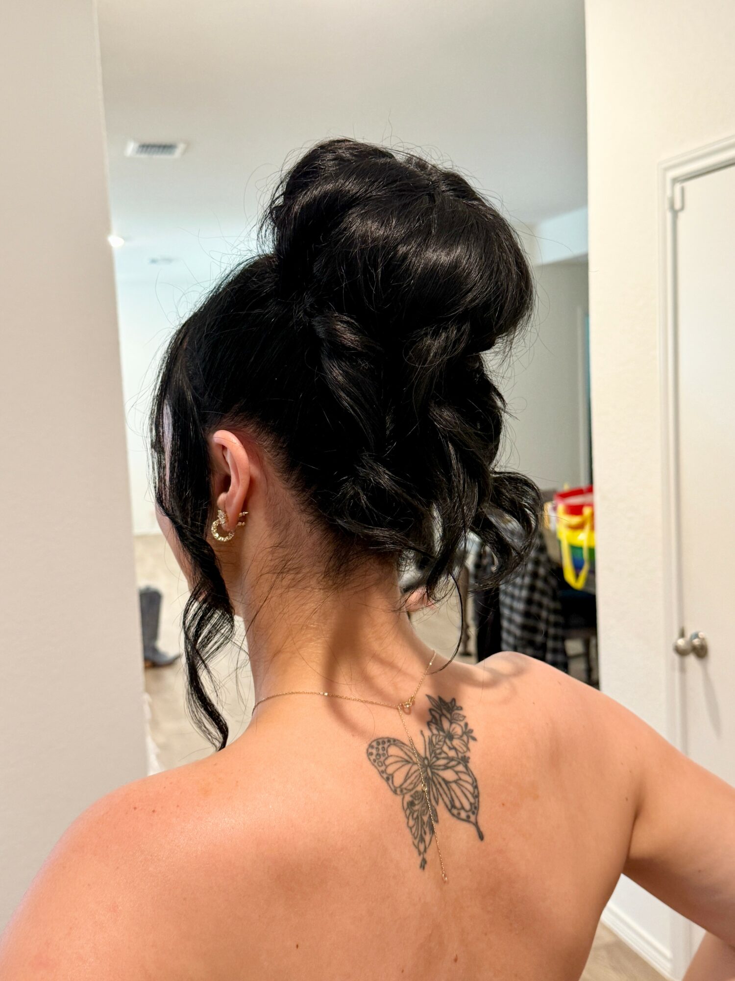 Back view of a woman with dark hair styled in an updo, showing a butterfly tattoo on her upper back.