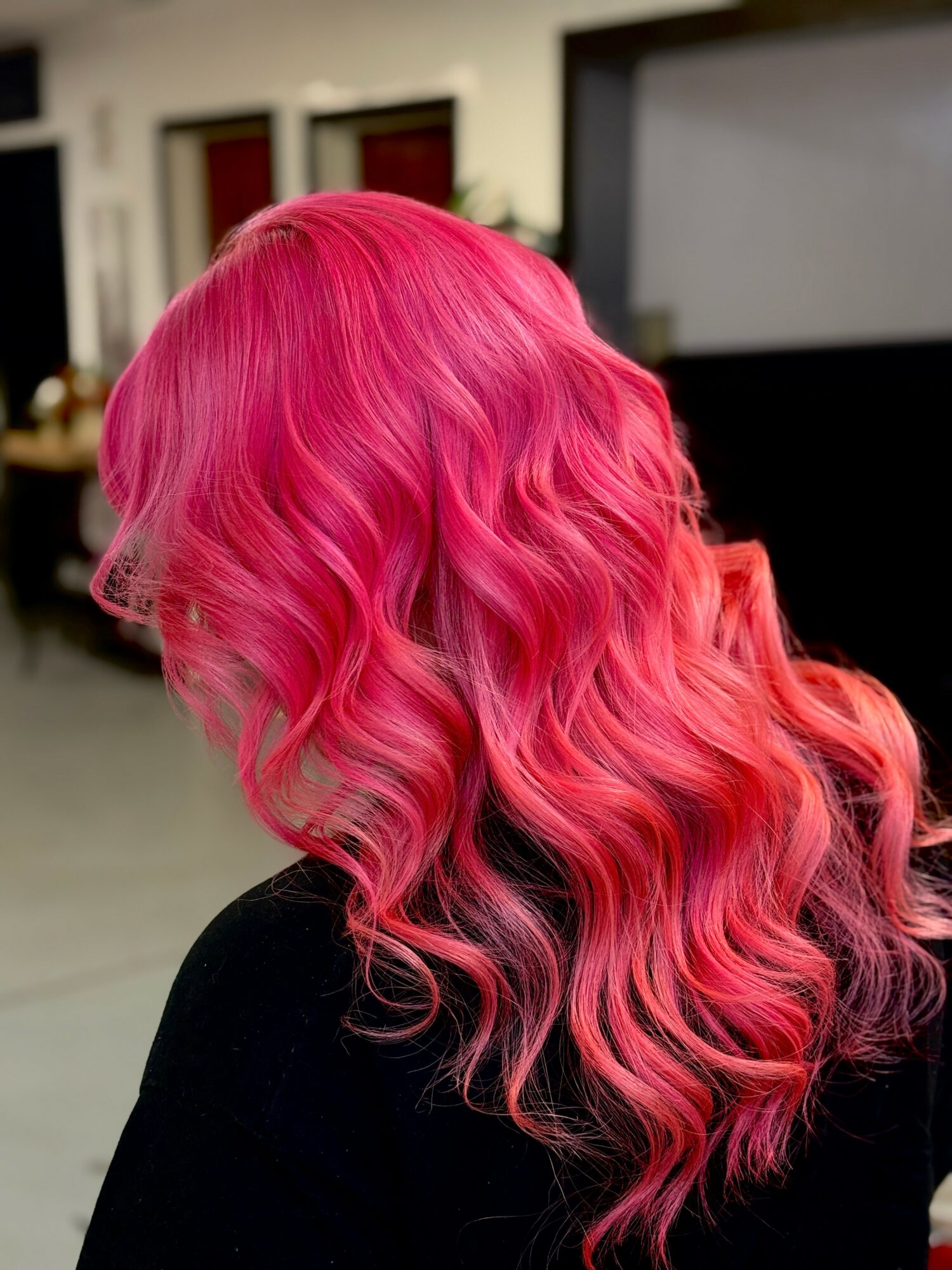 Person with vibrant pink, wavy hair seen from the back in an indoor setting.