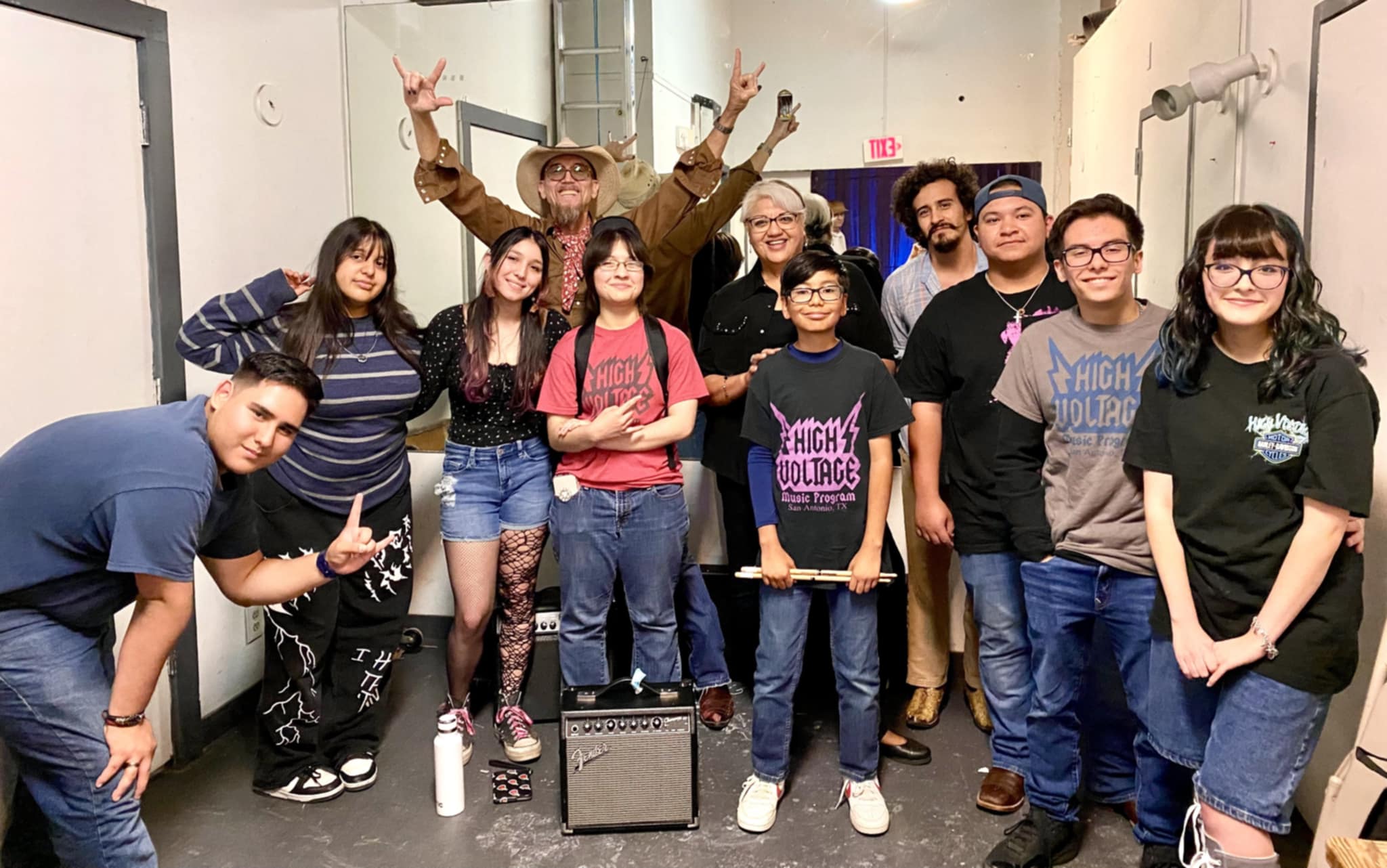 Group of ten people standing in a hallway, some smiling and making peace signs, with a person in a costume in the background.