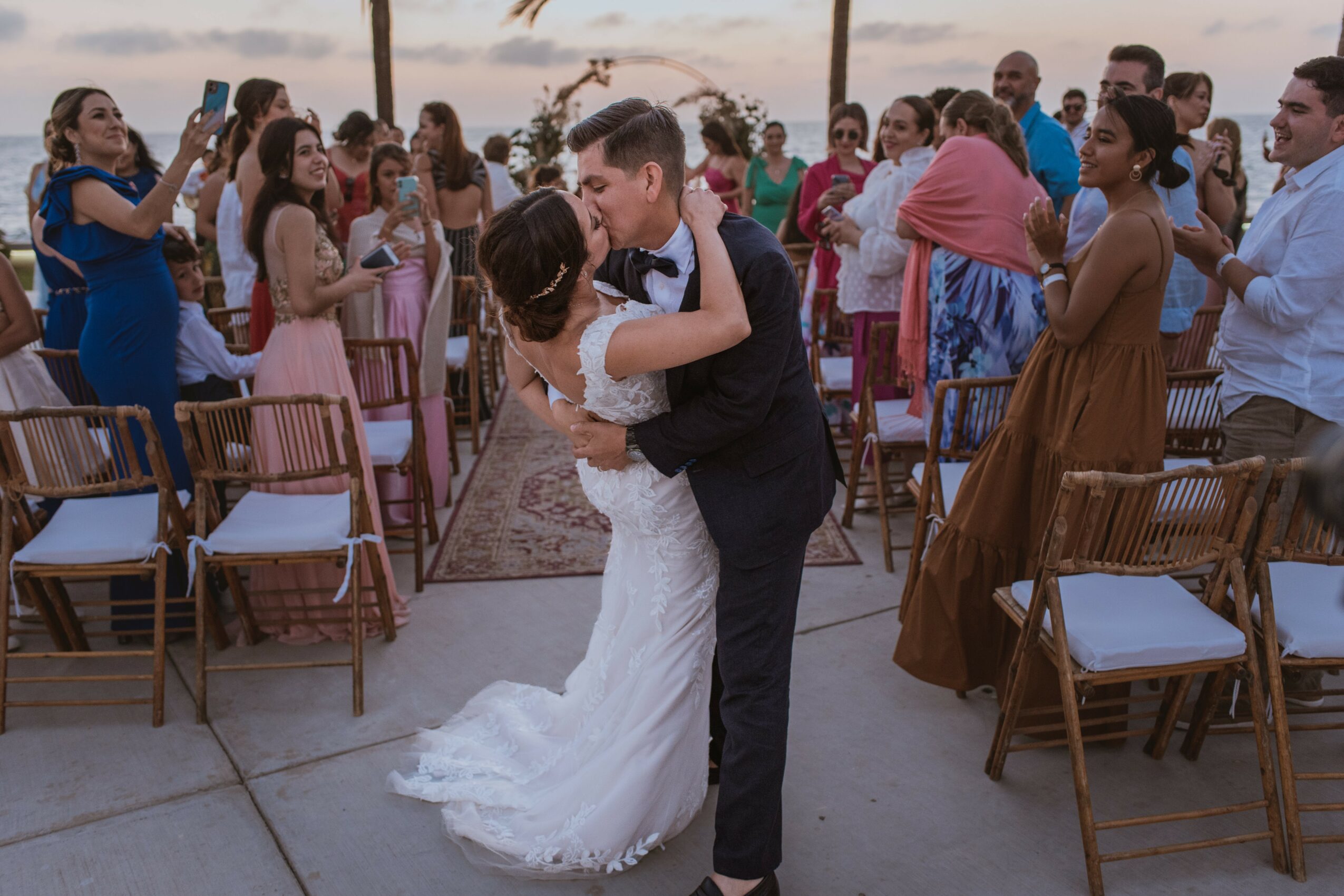 Couple dancing at wedding reception with guests watching and taking photos outdoors.