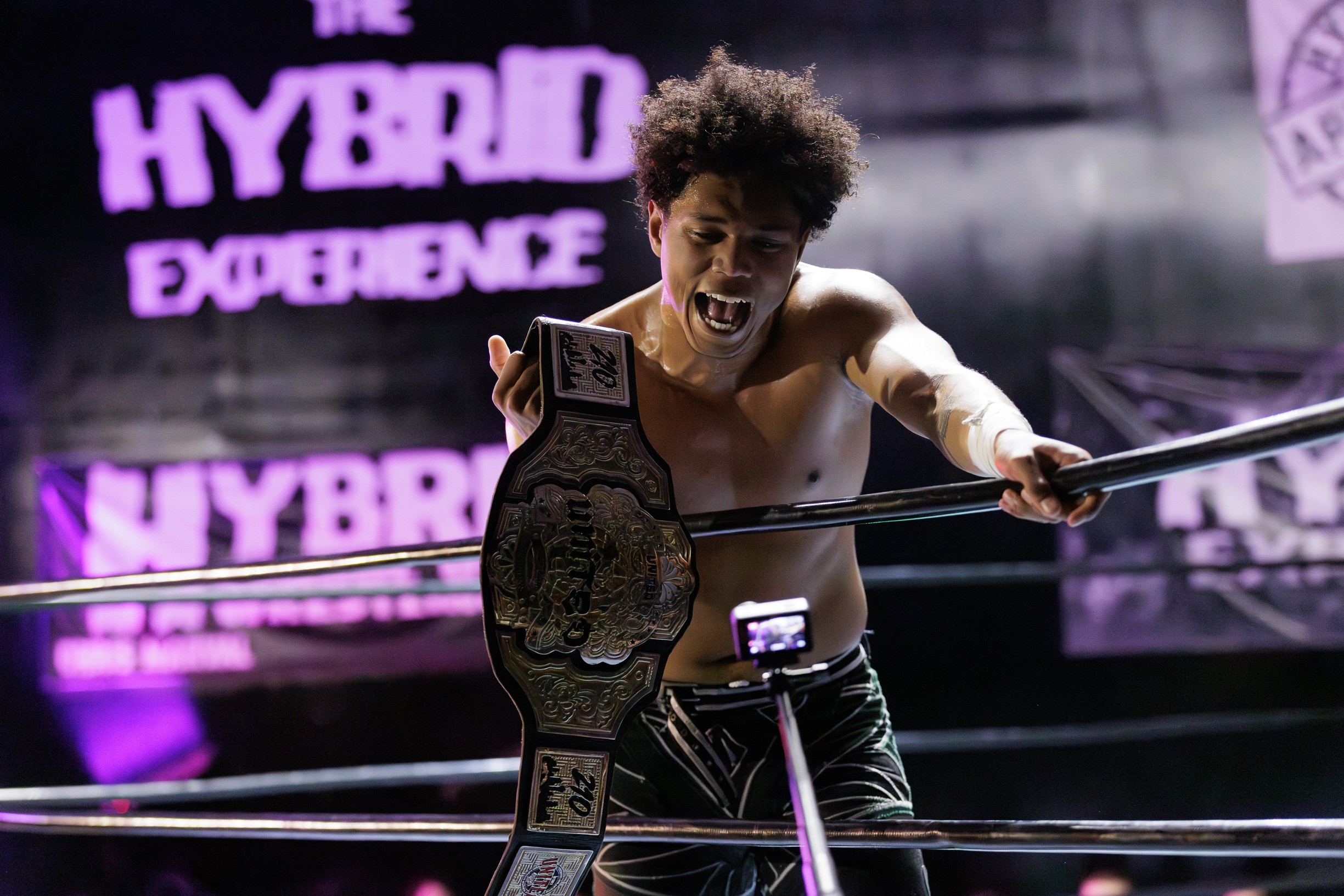 Young person in wrestling ring holding championship belt, celebrating victory, with purple-lit background and