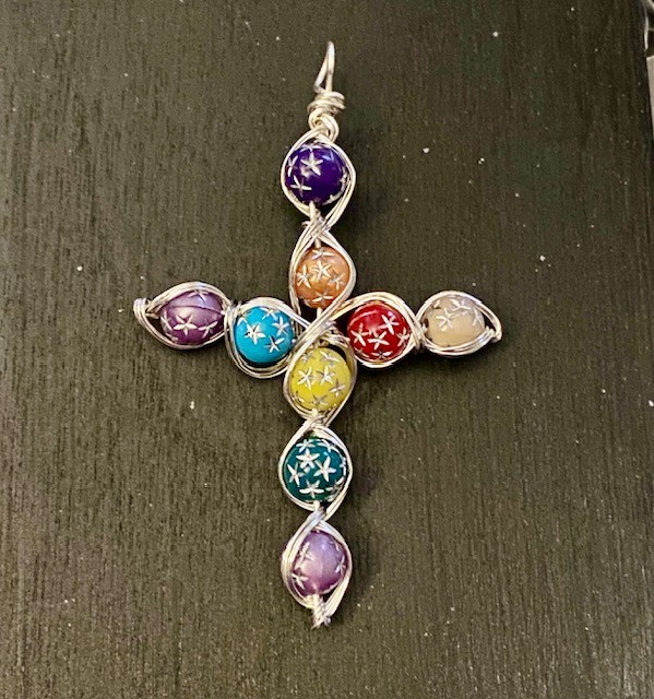 Colorful cross-shaped pendant with six circular sections, each with snowflake designs, on a dark surface.