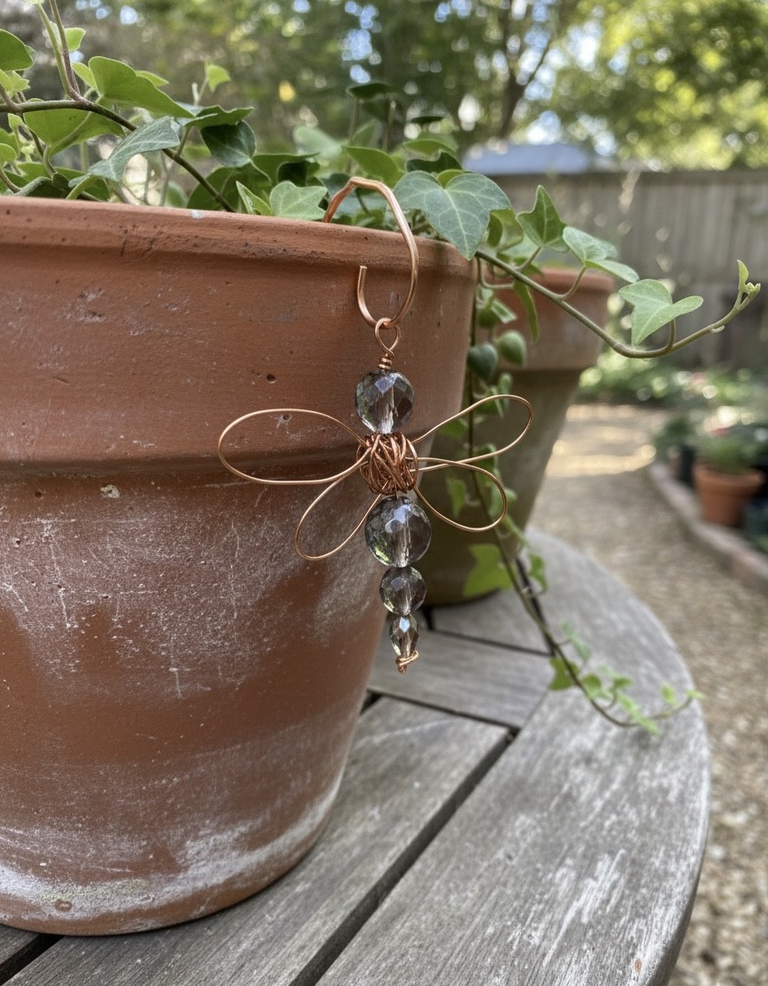 Decorative dragonfly ornament with glass beads on a plant pot outdoors, with a garden and trees in the background.