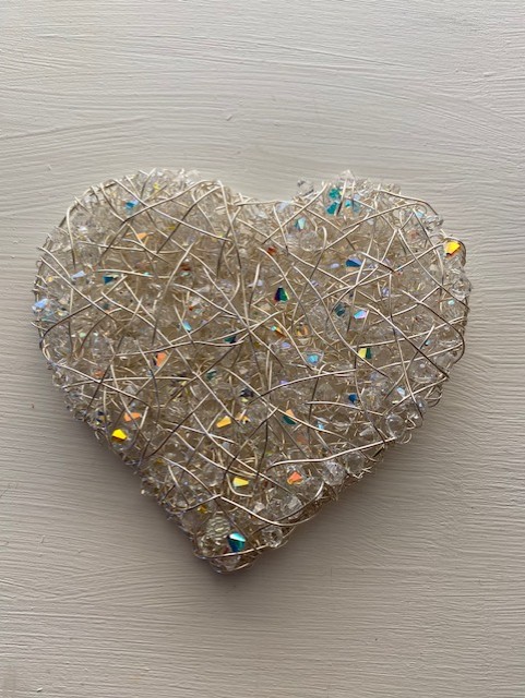 Heart-shaped wire sculpture with colorful beads, placed on a light-colored wooden surface.