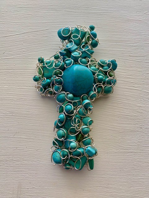 Turquoise beaded cross pendant with silver wire wrapping, on a light wooden surface.
