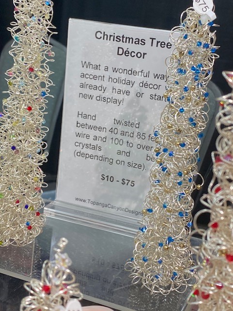 Two decorative Christmas trees made of silver wire with red, blue, and clear beads, displayed beside a sign.