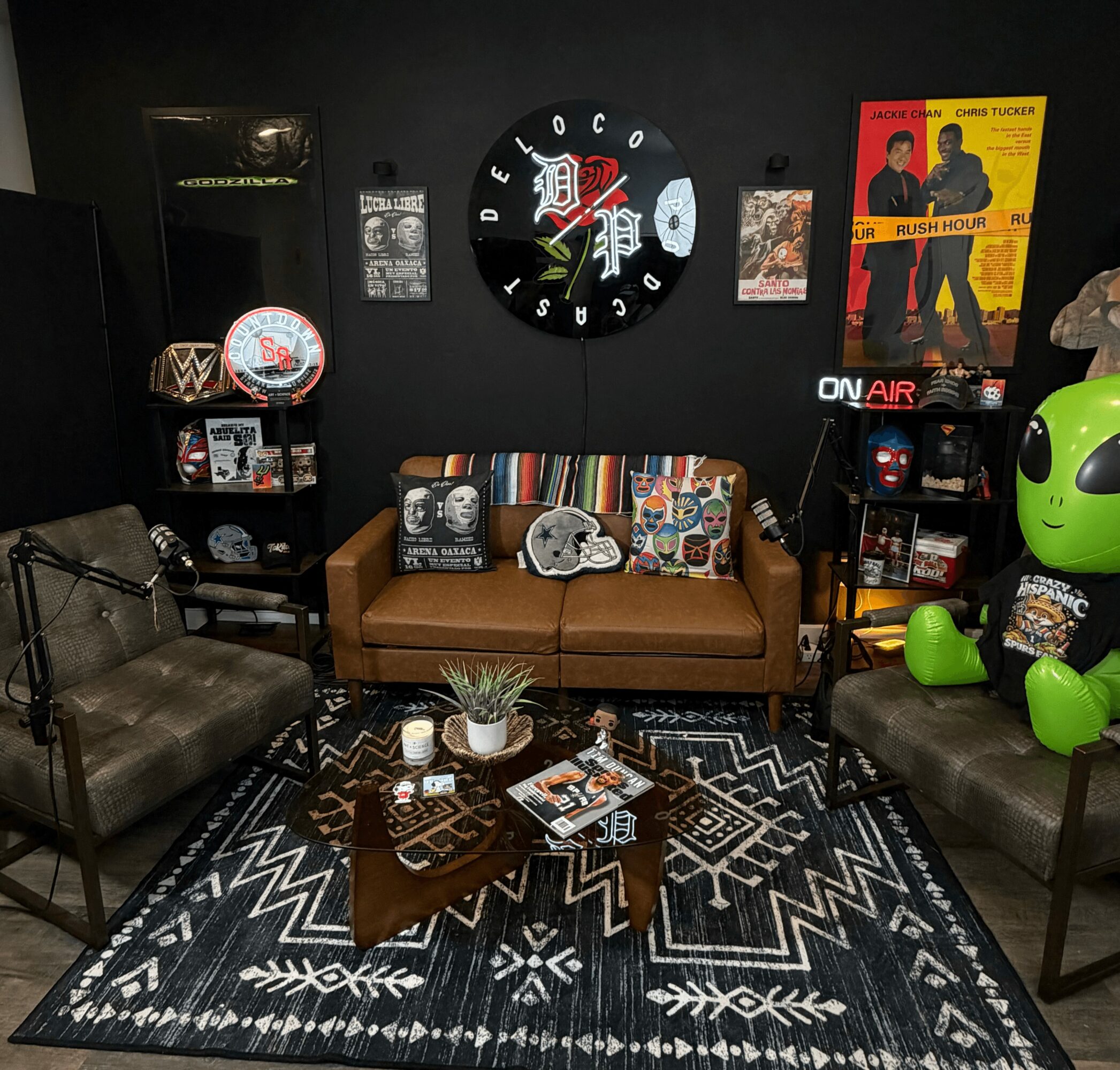 Cozy room with a brown sofa, black armchairs, a patterned rug, and various decorations including posters and a large green robot figure.