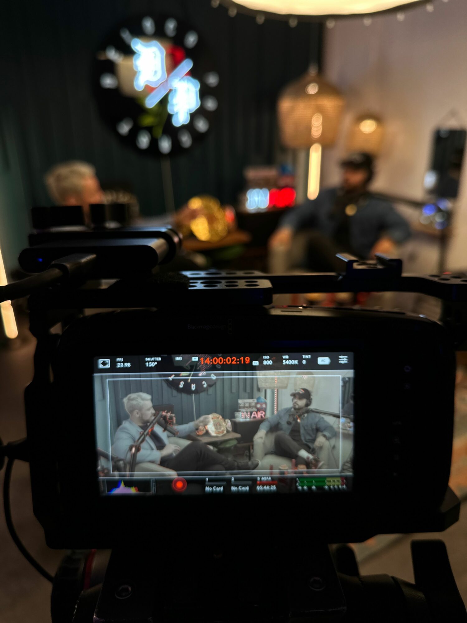 View through a camera screen showing people sitting at a table with drinks, in a dimly lit setting.