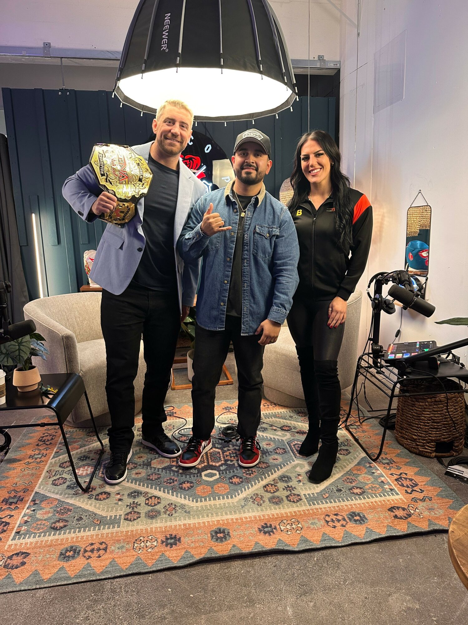 Four people standing indoors, one holding a bouquet, with a large lamp overhead and a patterned rug on the floor.