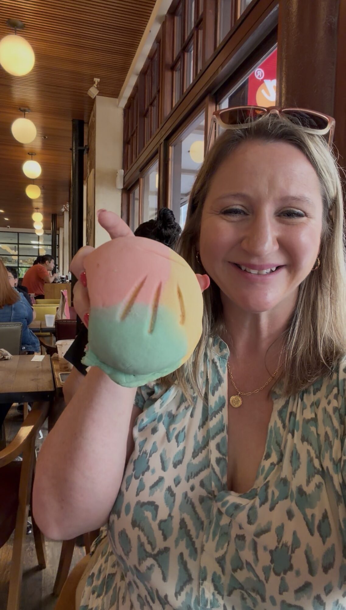 Woman smiling and holding a colorful cotton candy in a cafe setting.