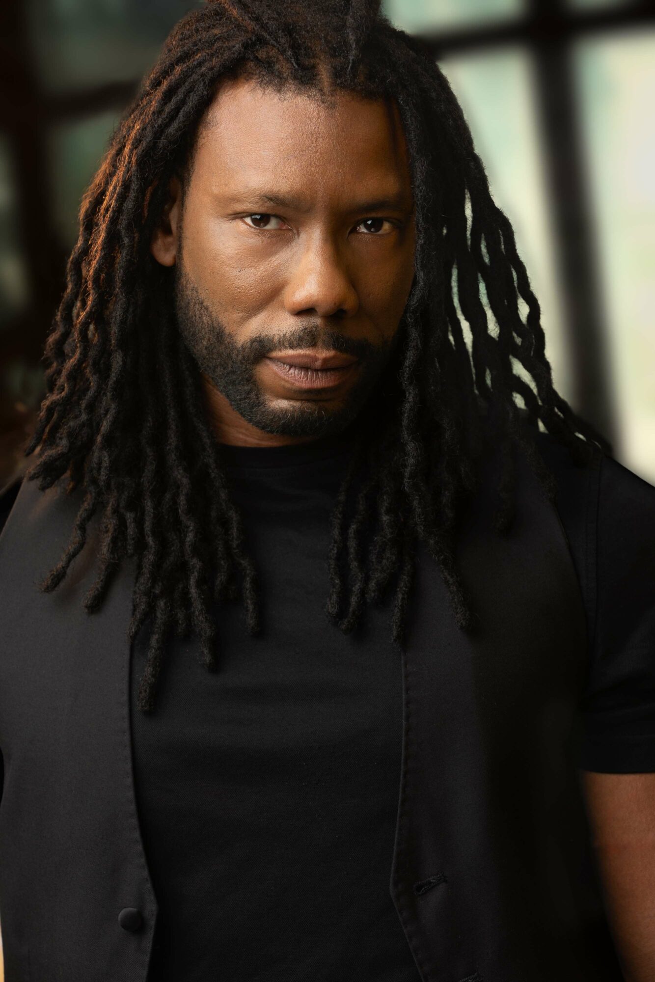 Man with long dreadlocks wearing a black shirt and jacket, looking directly at the camera.