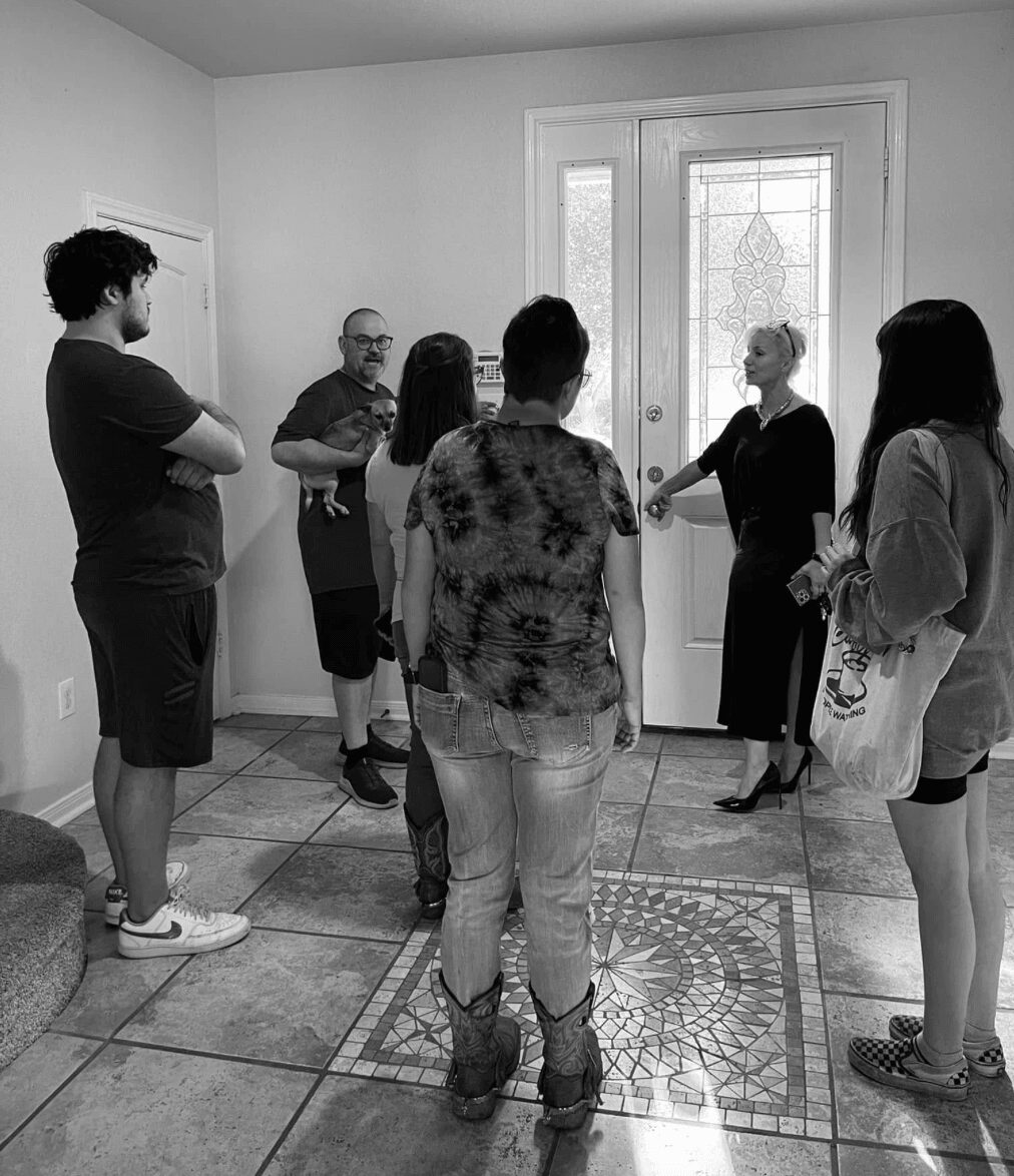 Group of seven people standing inside a room near a door with glass panels, engaged in conversation, some with arms crossed.