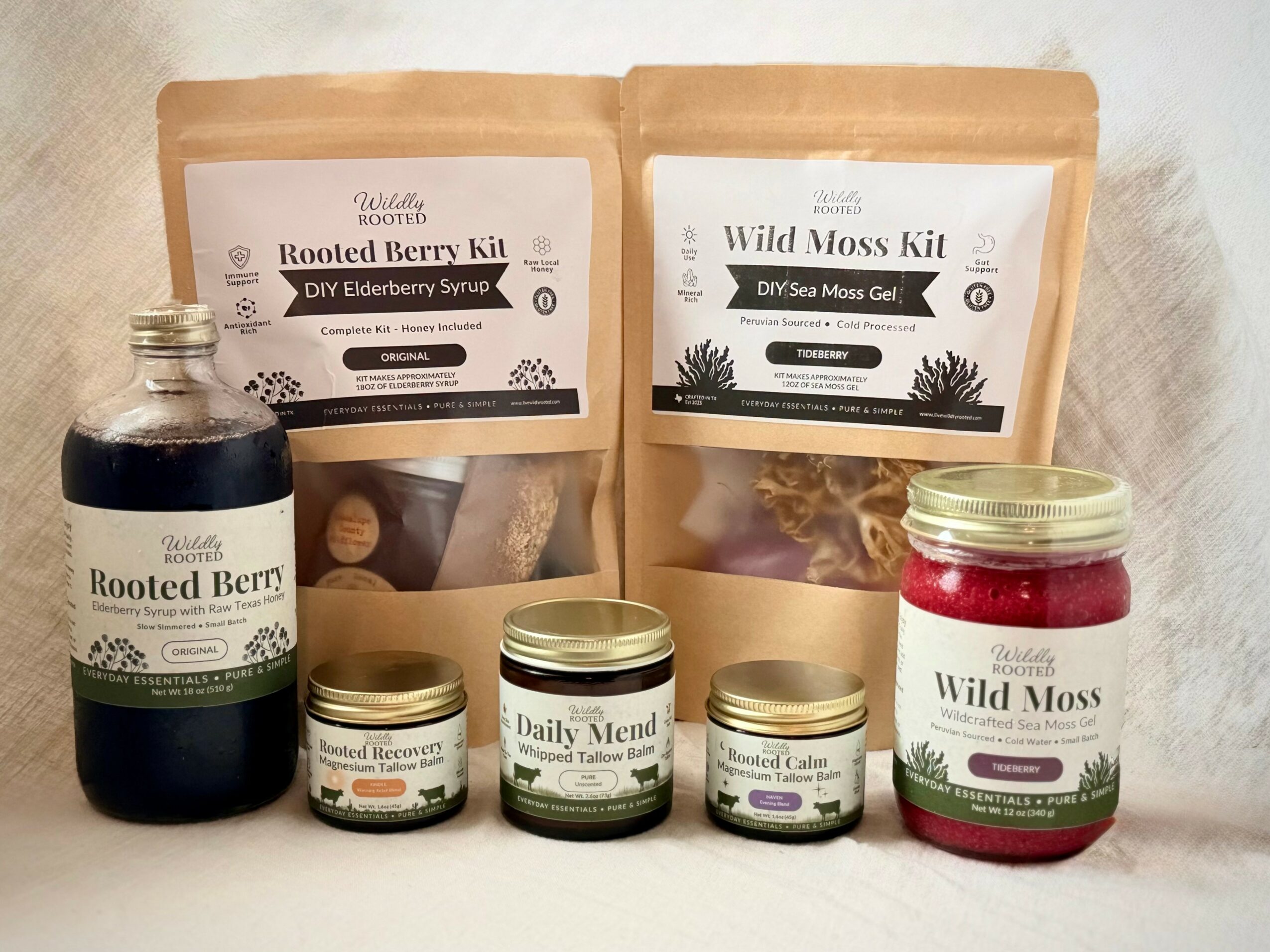 Six natural product packages and jars, including root berry kit, moss kit, and herbal remedies, arranged on a white surface.