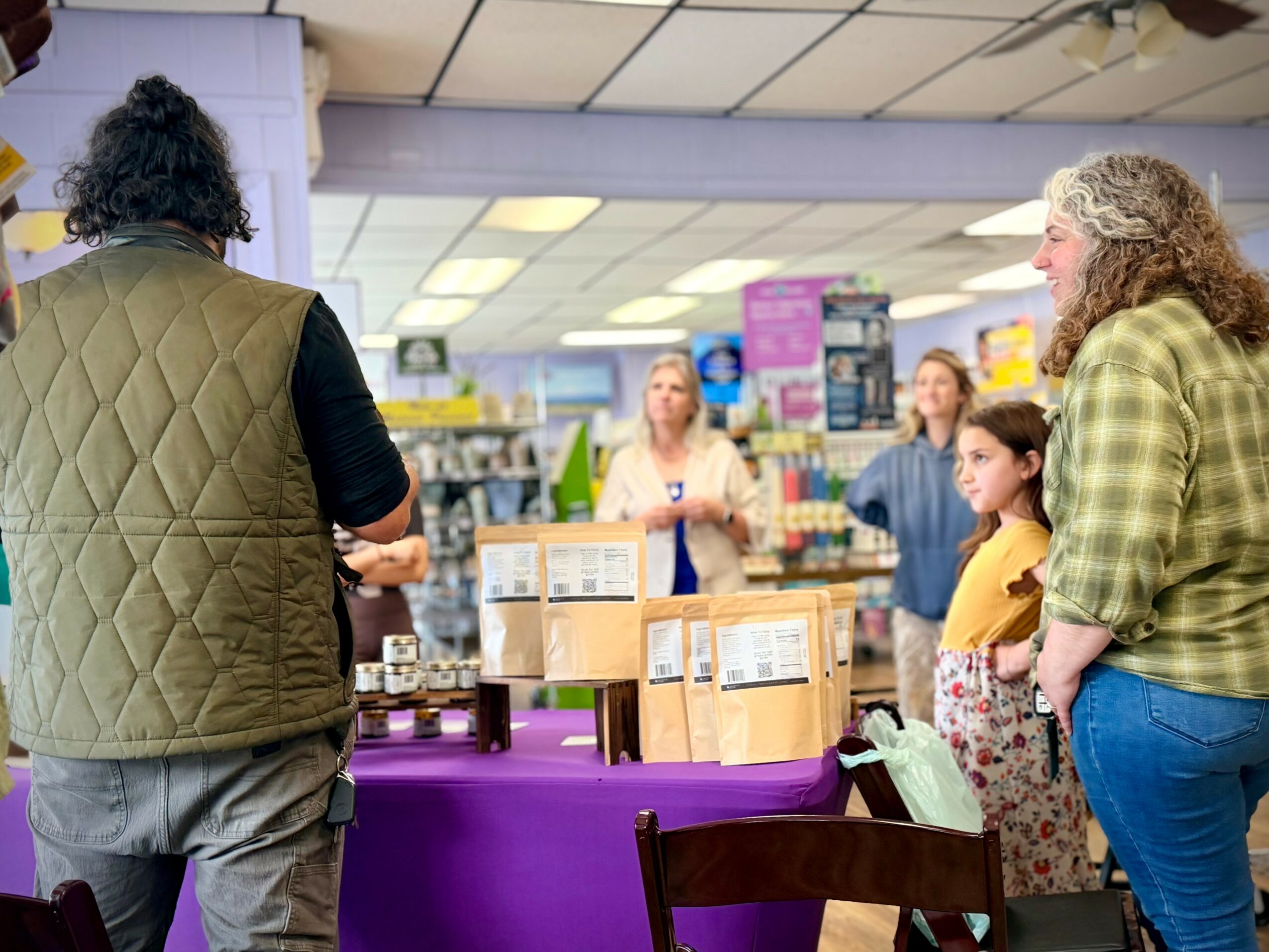 People in a store listening to a person speaking, with shelves and products in the background.