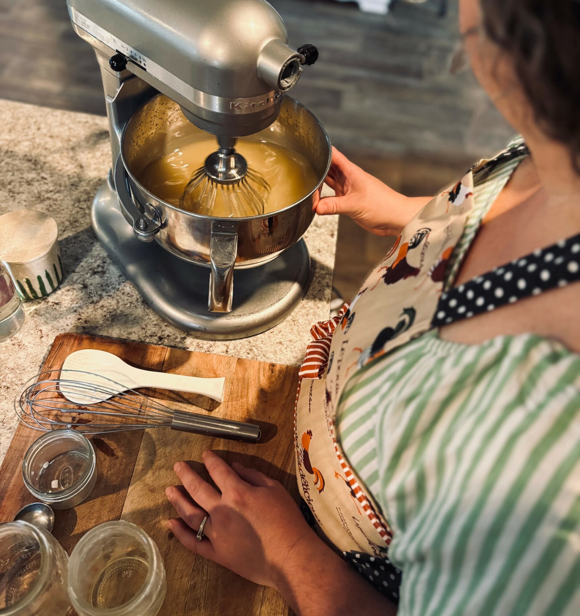 Person using a stand mixer to beat batter in a kitchen, with baking tools on a wooden countertop.