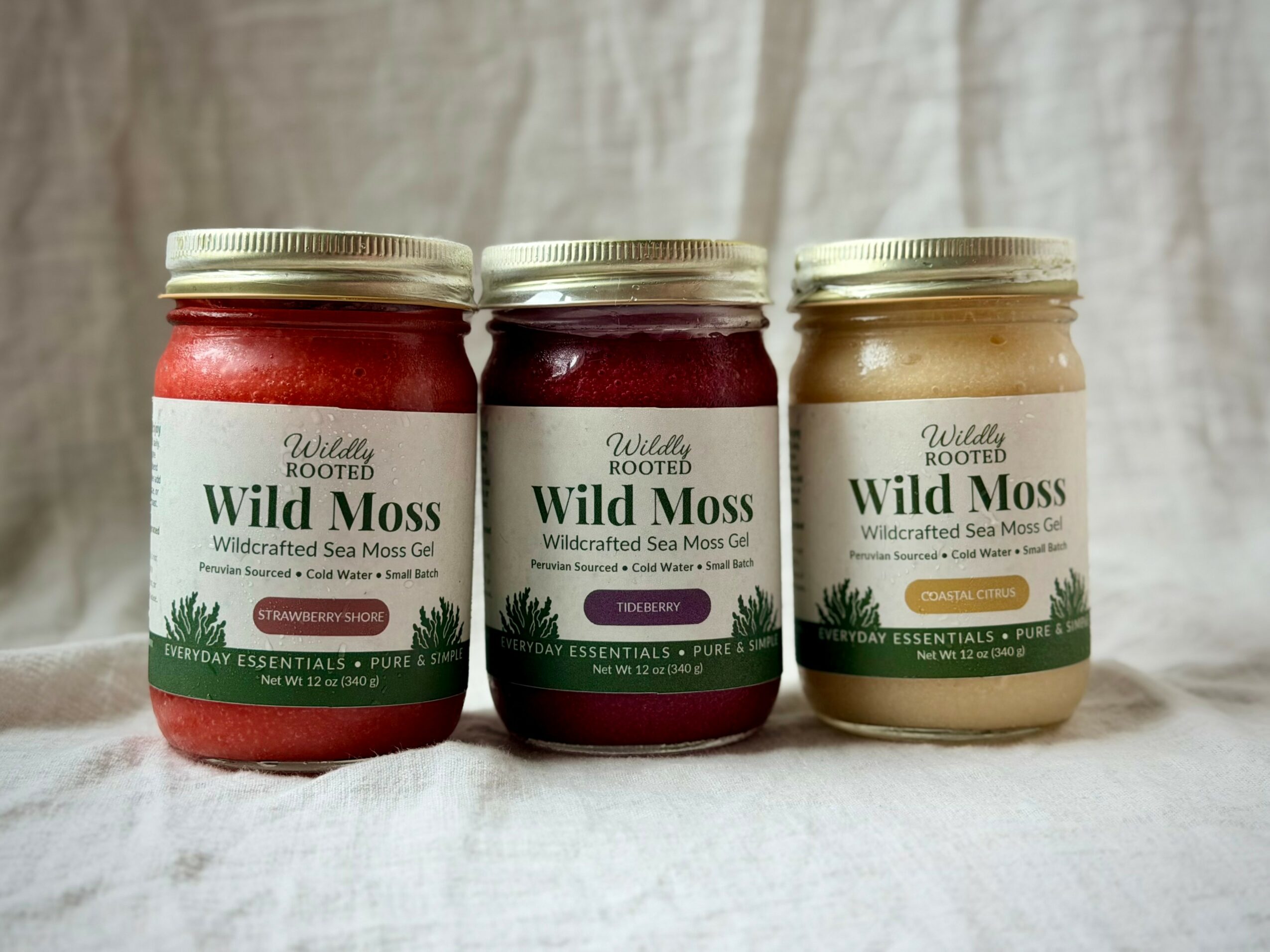 Three jars of Wild Moss herbal product with silver lids, labeled with green and white, placed on a fabric background.