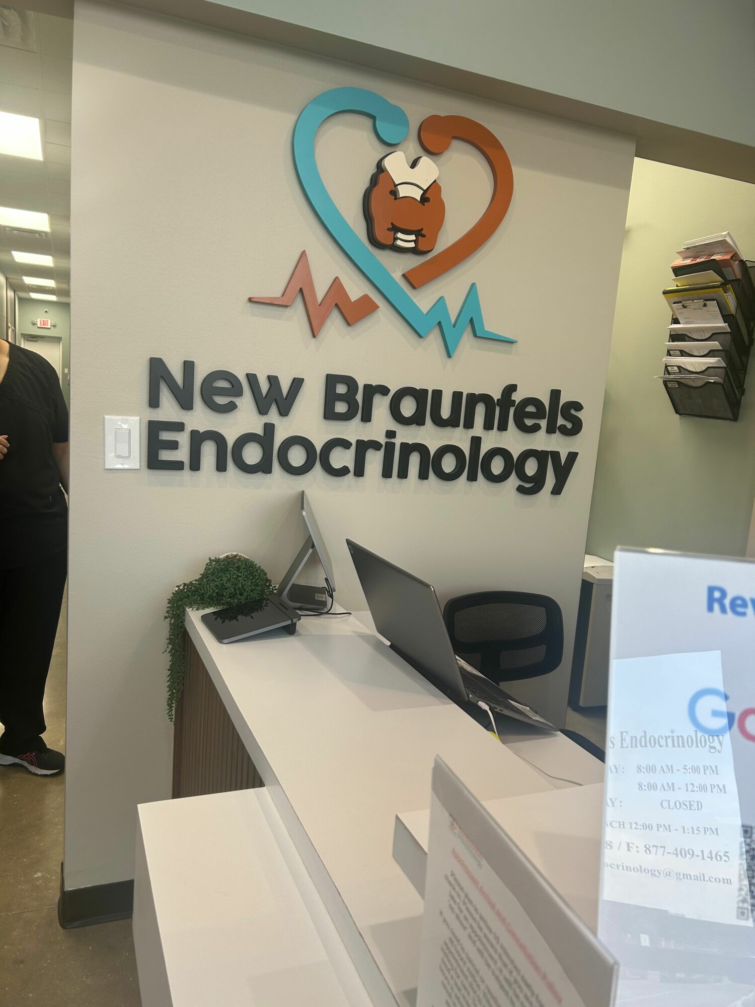 Reception area with sign reading 'New Braunfels Endocrinology' and logo, a desk with a laptop, and informational materials.