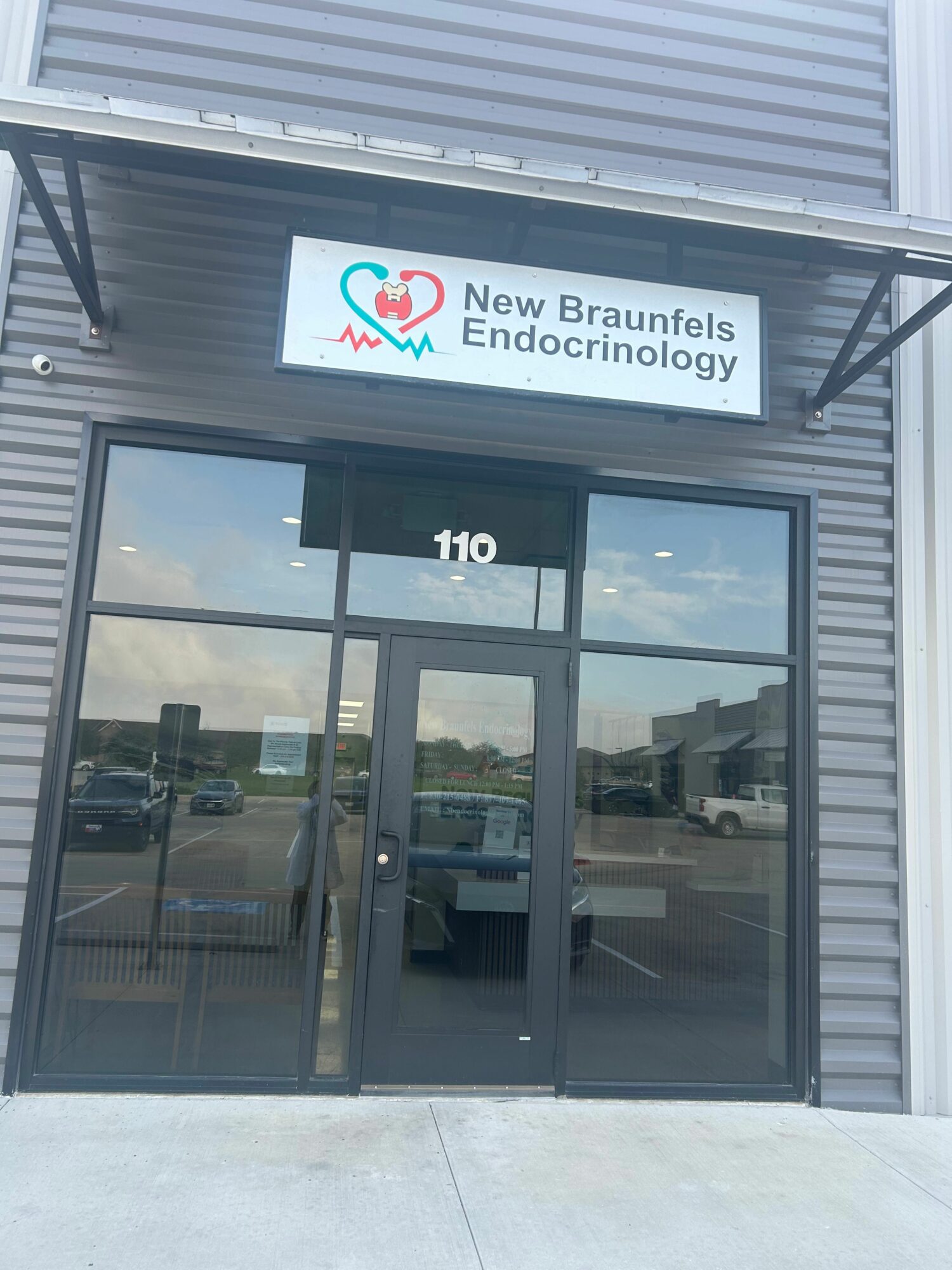 Glass door with a sign for New Braunfels Endocrinology, reflecting the outside view, including a building and sky.