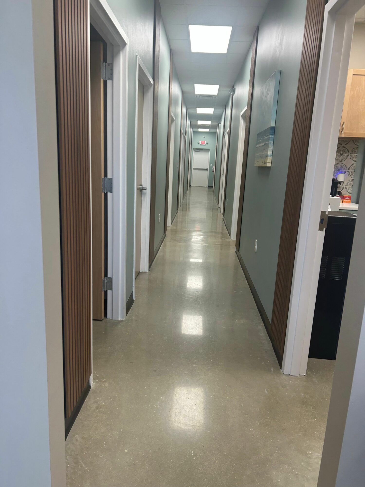 Long corridor with multiple doors, bright lighting, and a polished floor, viewed from the side.