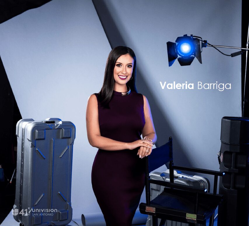 Woman in a sleeveless dark purple dress standing in a studio with a suitcase and camera equipment, smiling.