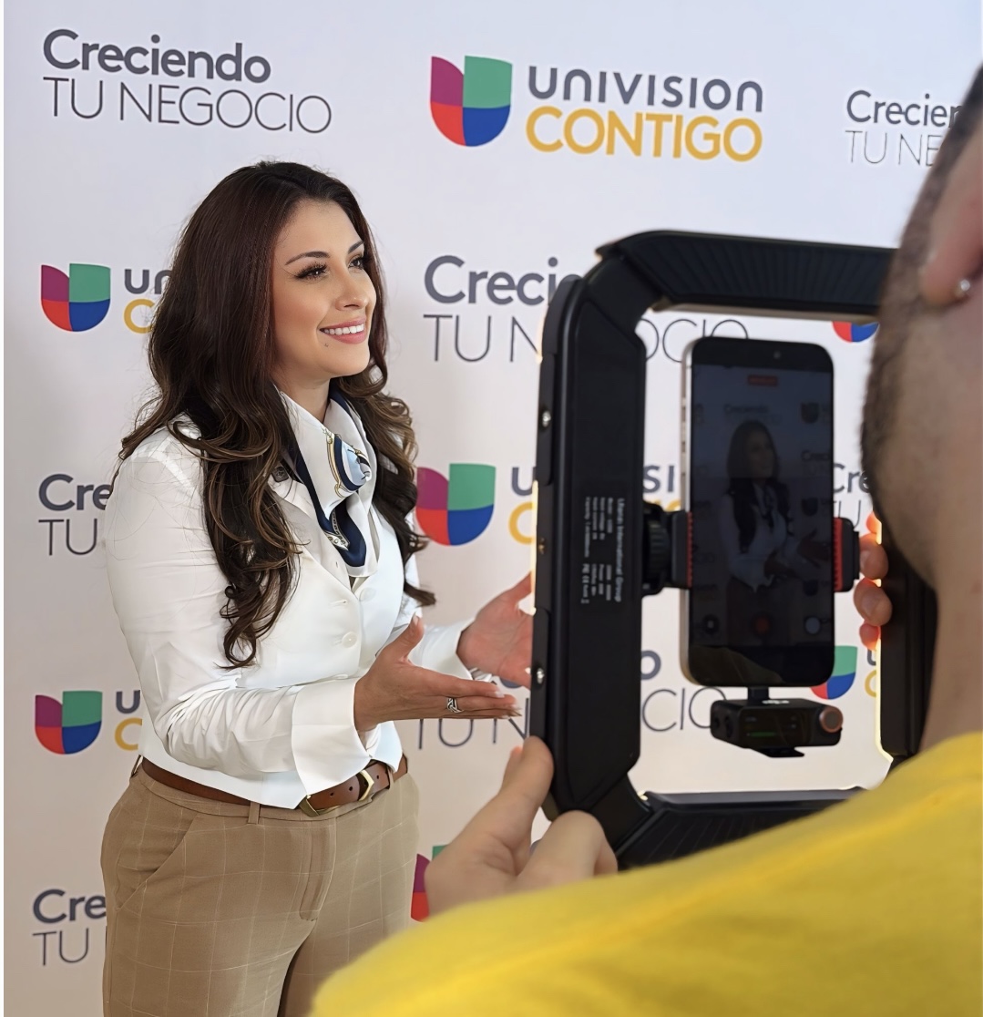 Woman with long dark hair smiling and gesturing during an interview, background with Univision logos and text.