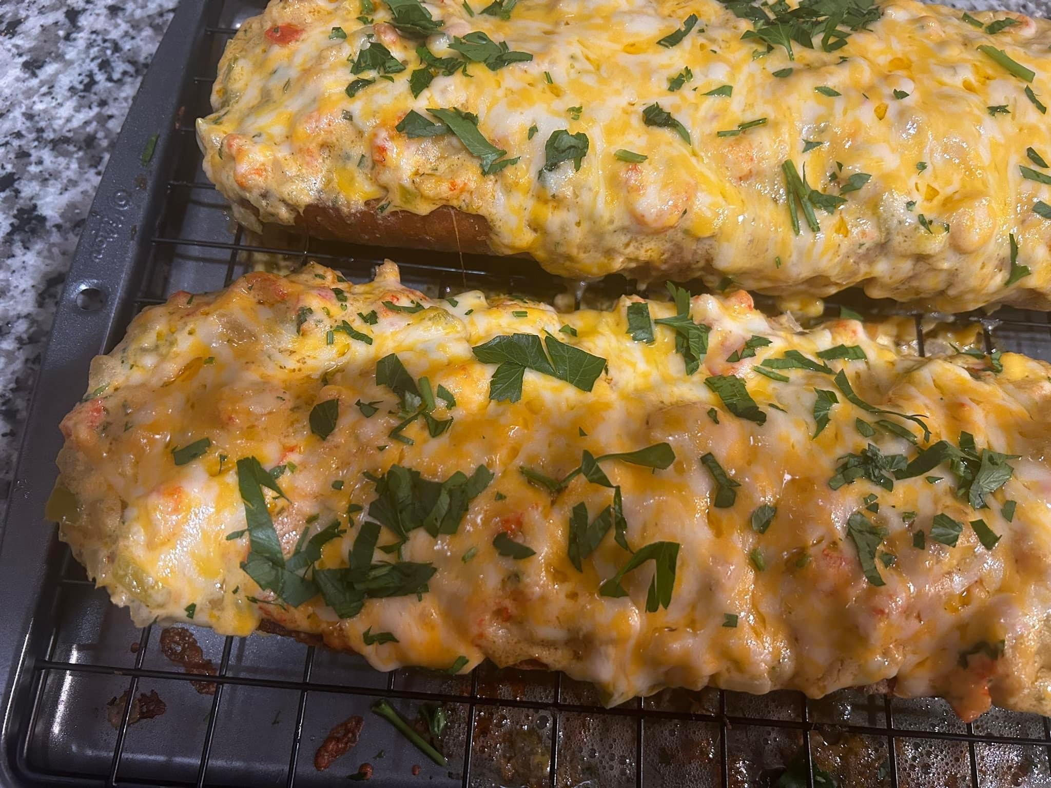 Two baked fish fillets topped with melted cheese and chopped herbs on a wire rack.