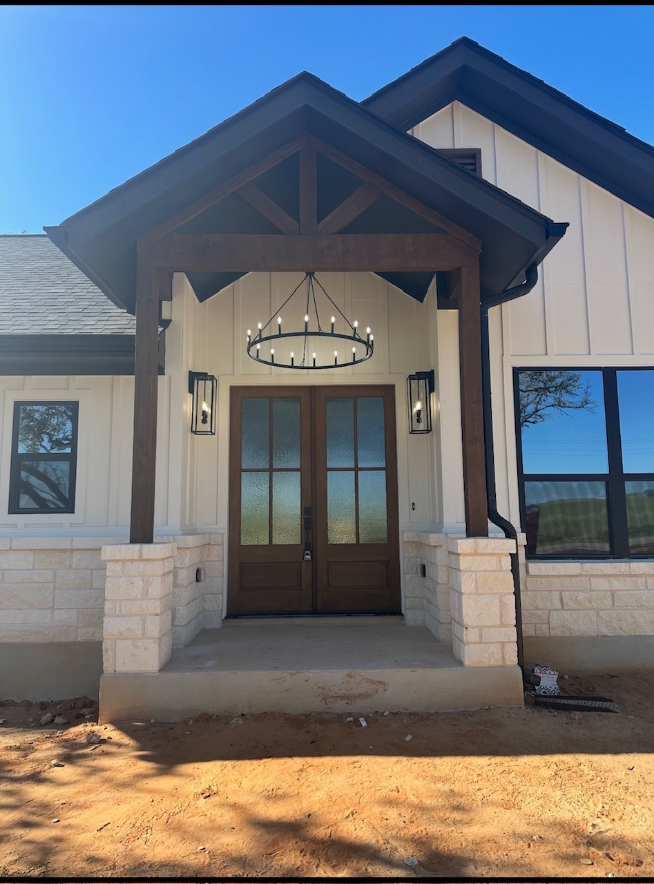 Front entrance of a house with double glass doors, wooden accents, and a circular chandelier, under a gabled roof.