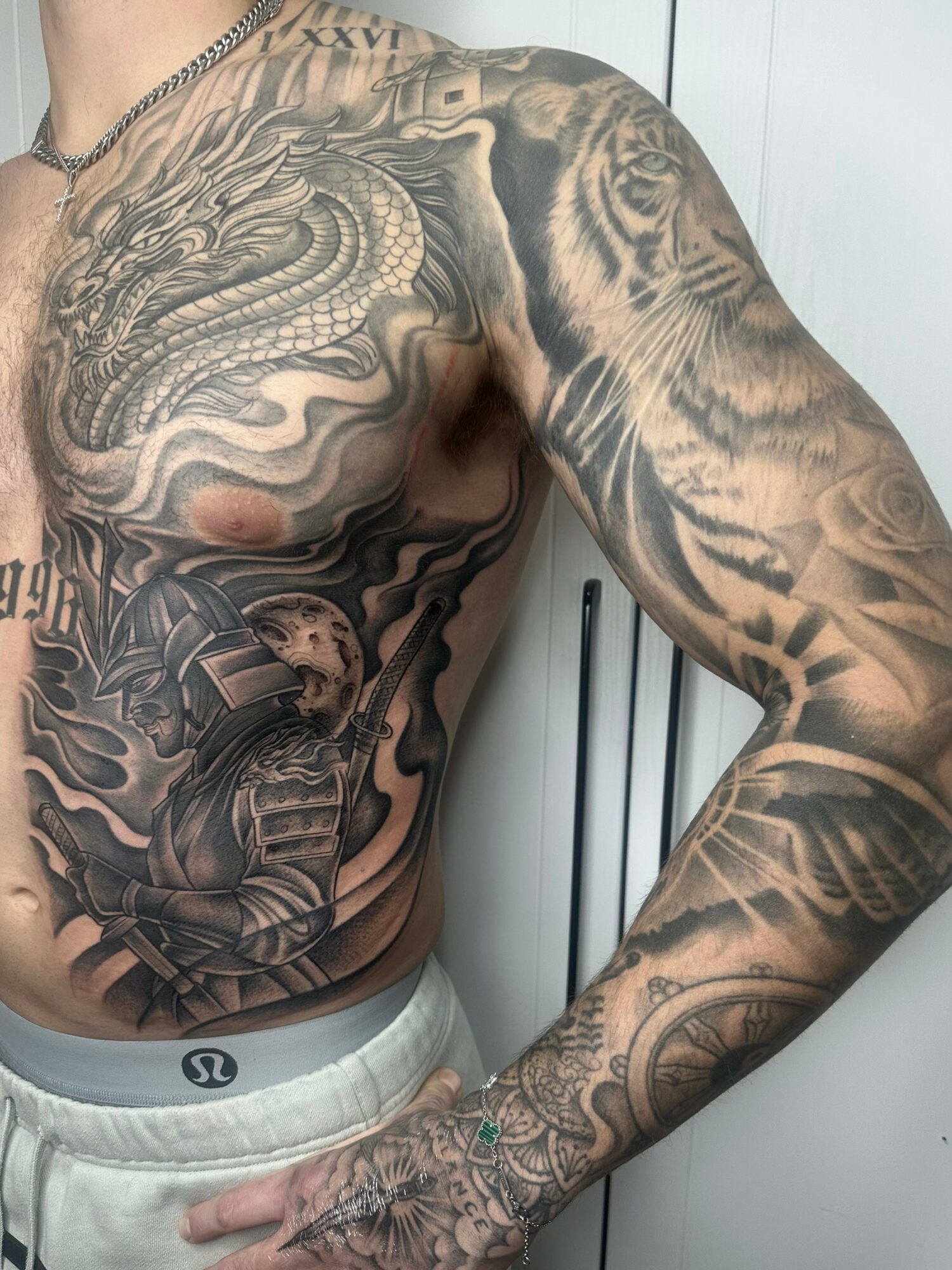 Close-up of a person's upper body and arm with detailed black and gray tattoos, including a dragon and tiger.