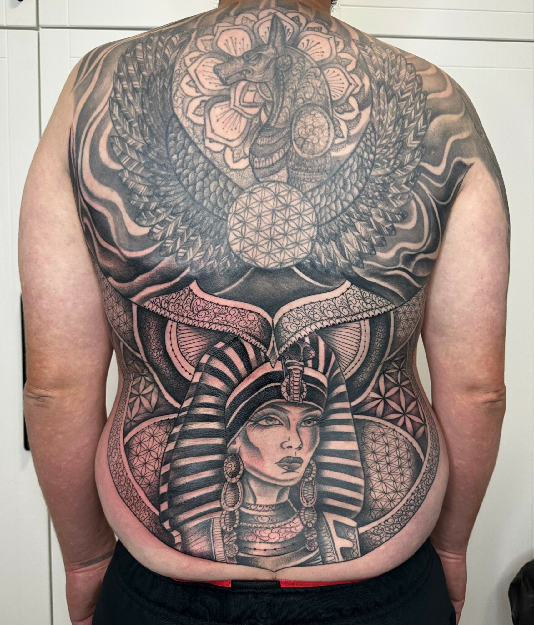 Back tattoo featuring a woman with Egyptian headdress, surrounded by intricate patterns and a large snake, covering the entire back.