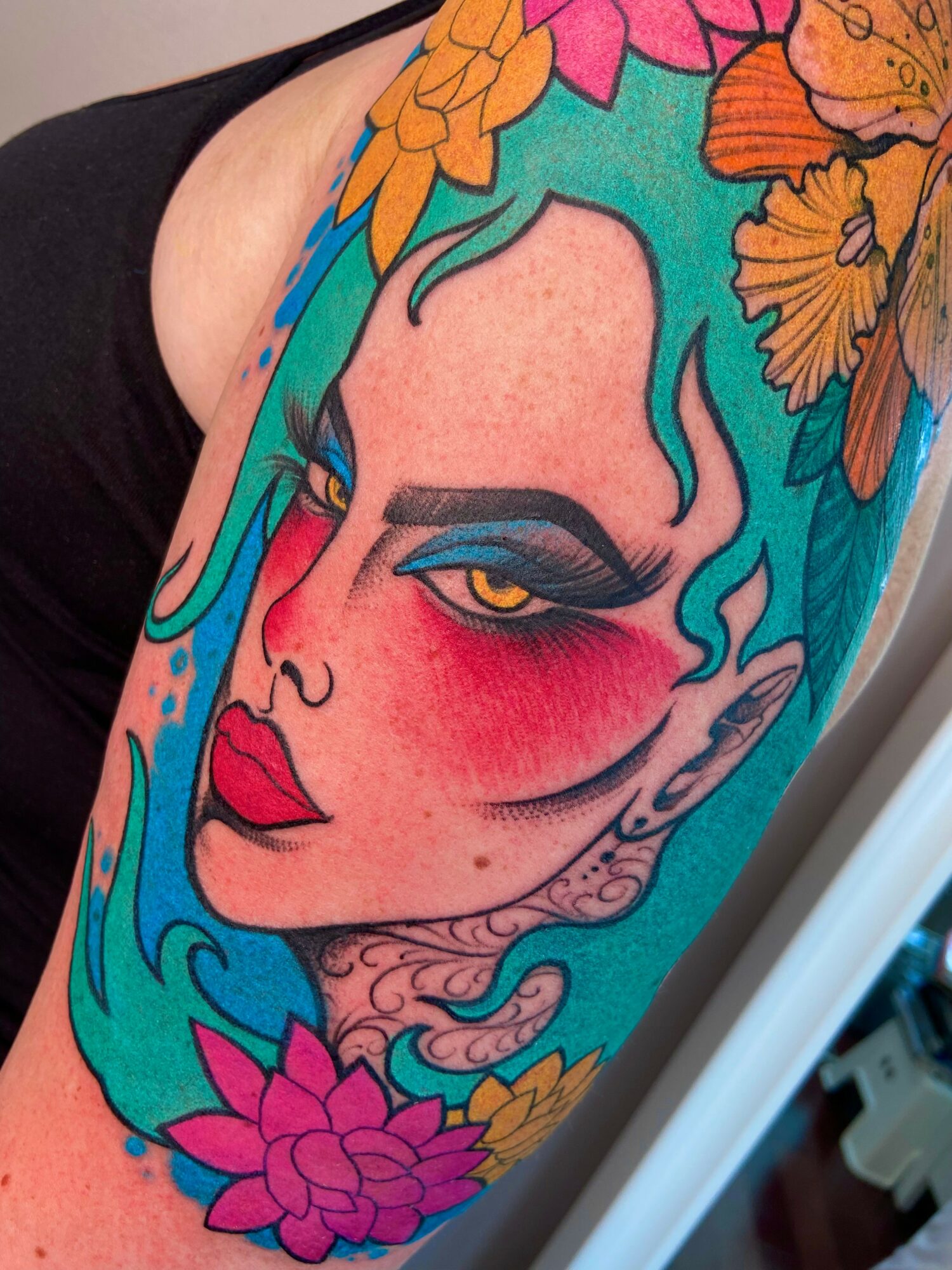 Tattoo of a woman's face with colorful flowers and flowing hair, featuring bold makeup and vibrant colors.