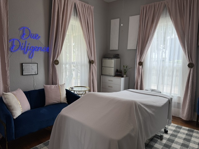 Room with a bed, a blue sofa with pillows, pink curtains, a white dresser, and a neon sign reading 'Dua Diliquna'.