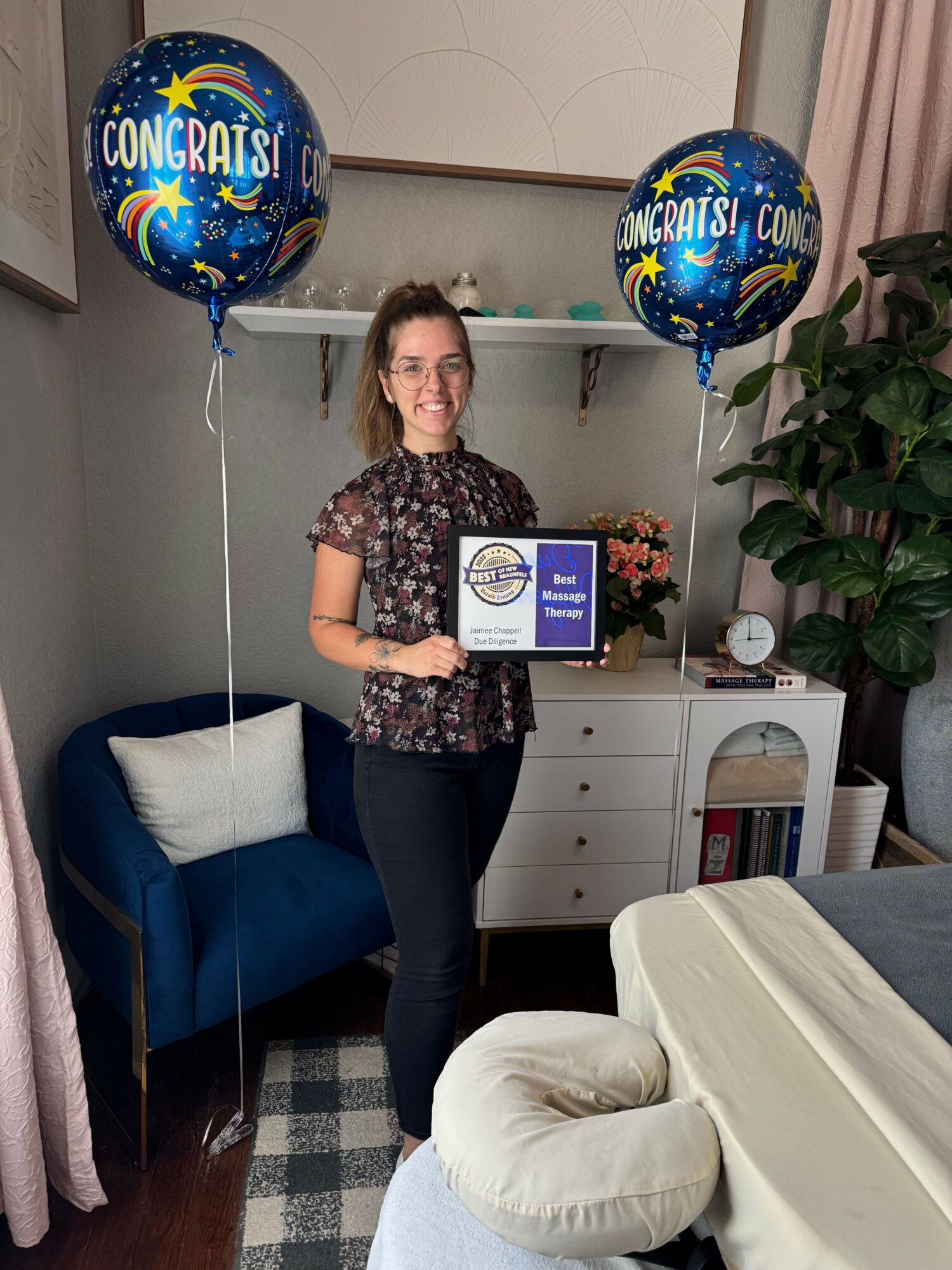 Woman holding a congratulatory certificate standing in a room with balloons and furniture.