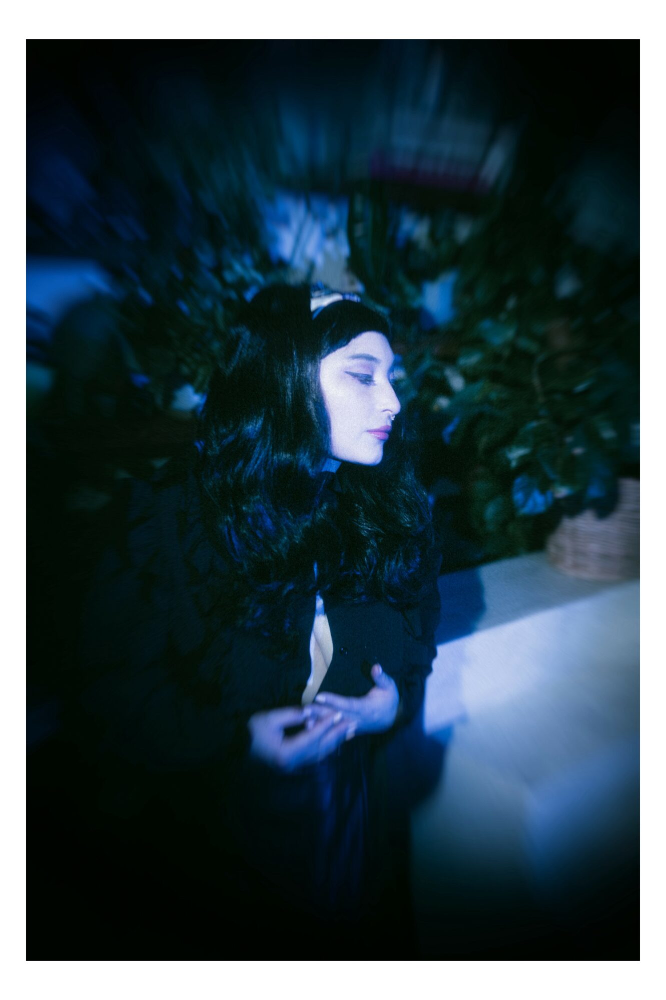 Woman with long dark hair and makeup, standing outdoors at night, surrounded by foliage, with a focused expression.
