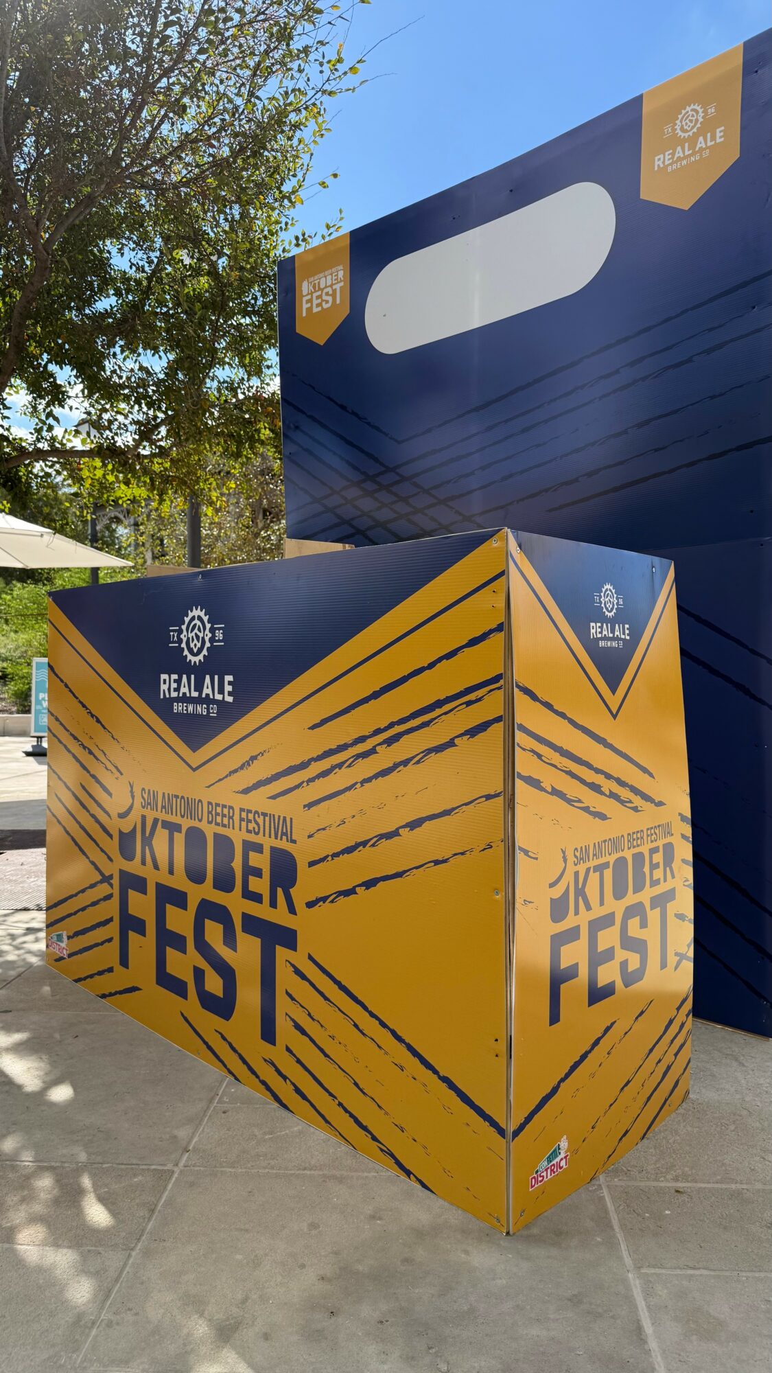 Orange and blue box with October Fest text, outdoors with trees and blue sky, sunlight casting shadows.