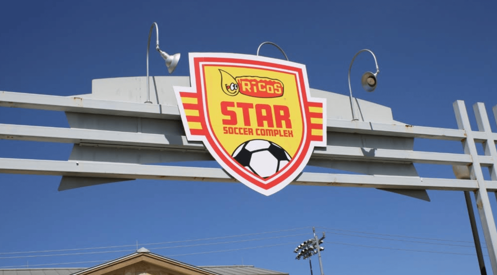 Sign for Ricos Star Soccer Complex with a soccer ball logo and blue sky background.