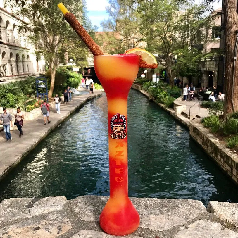A large cocktail glass-shaped inflatable with a straw, lemon slice, and colorful design, placed on a stone ledge by a canal.