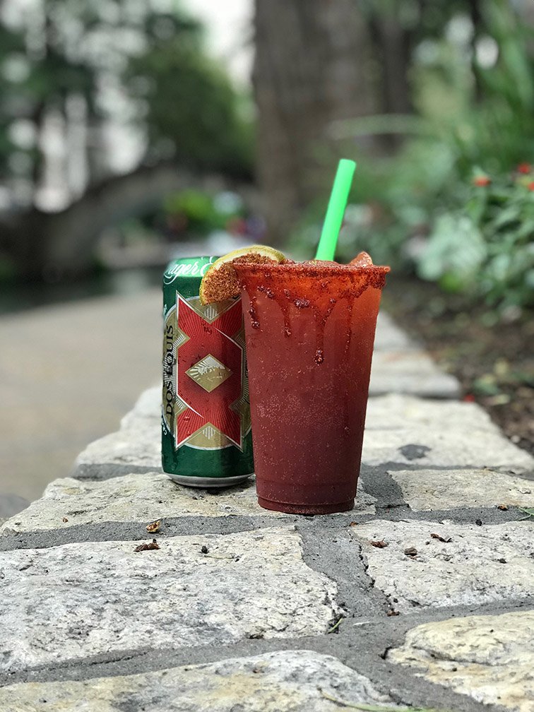 A red drink with a green straw and a cookie on top, next to a can, on a stone surface outdoors.