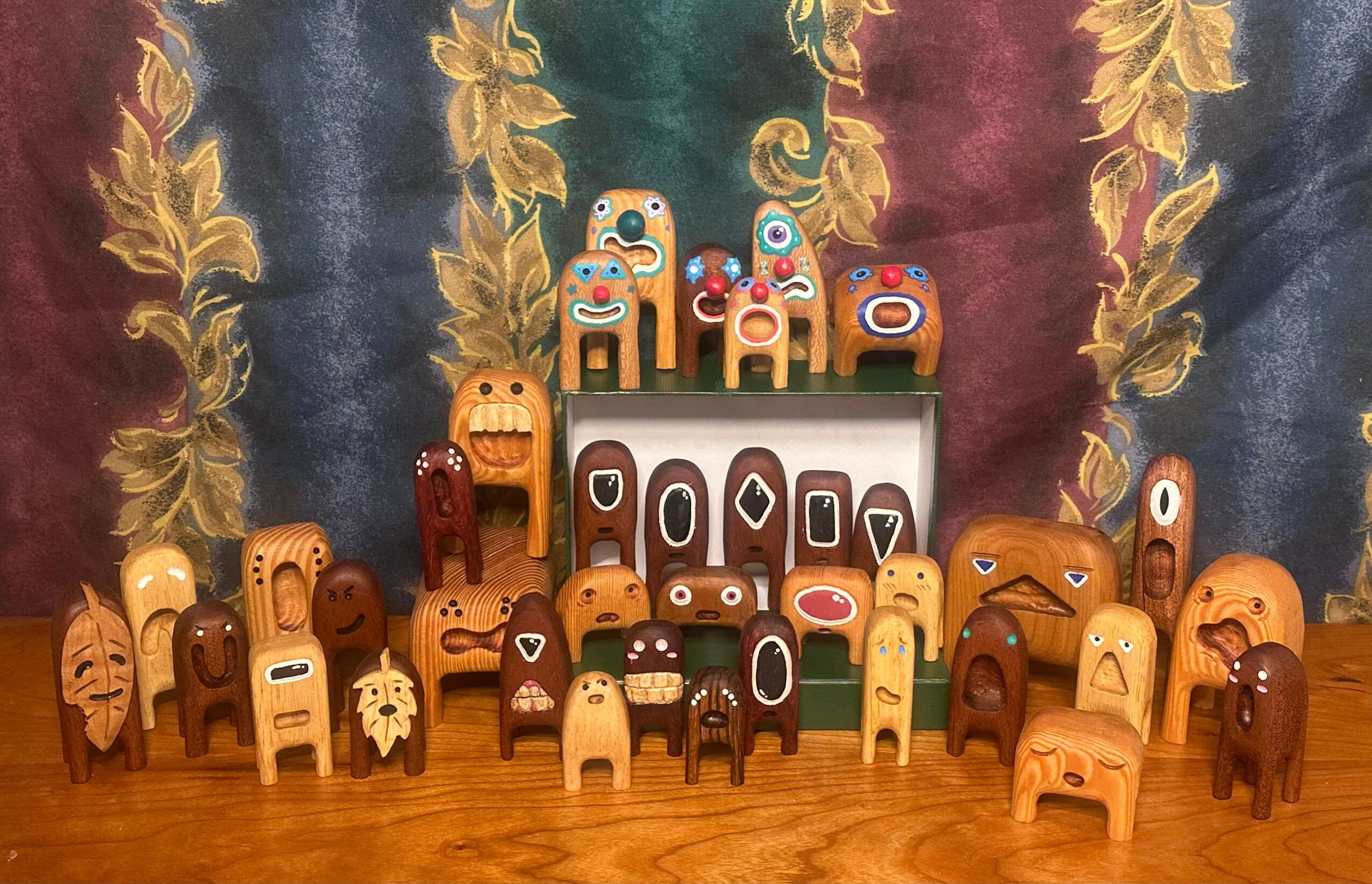 Collection of colorful, carved wooden animal figures arranged on a wooden surface with a decorative fabric background.