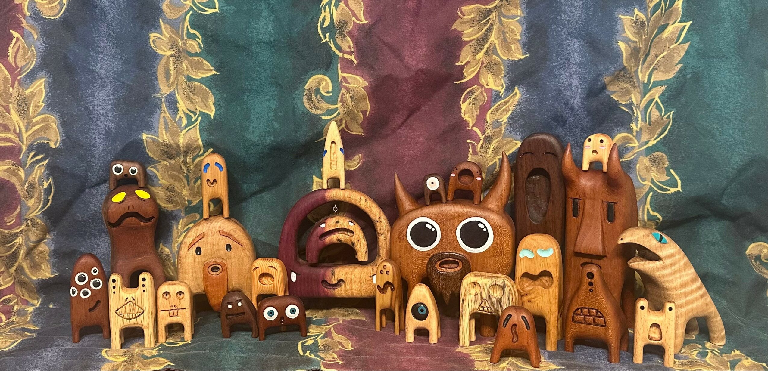 Collection of small wooden animal and creature figurines arranged in front of a colorful fabric backdrop.