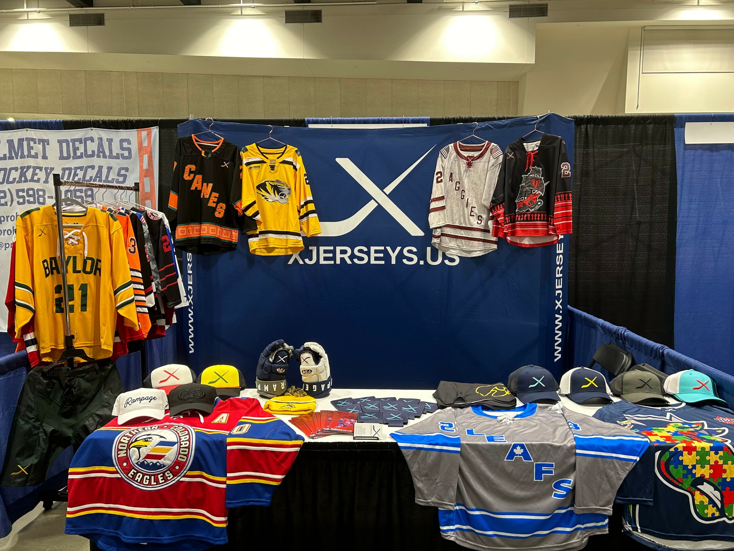 Display of hockey jerseys, hats, and merchandise on tables at an event booth with a blue backdrop.