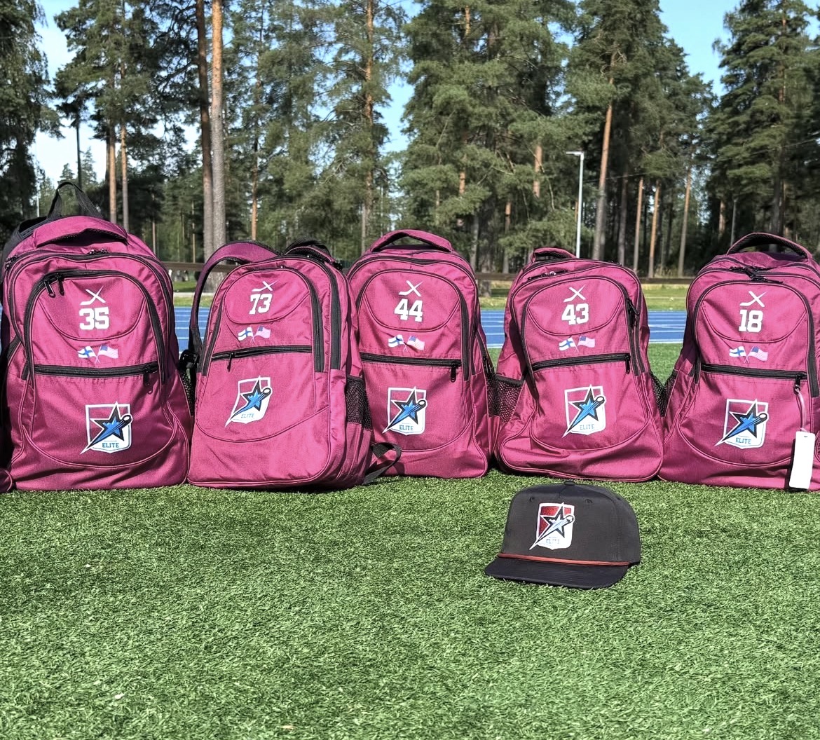 Five pink backpacks with numbers and logos are lined up on grass, with a black cap in front, trees in background.