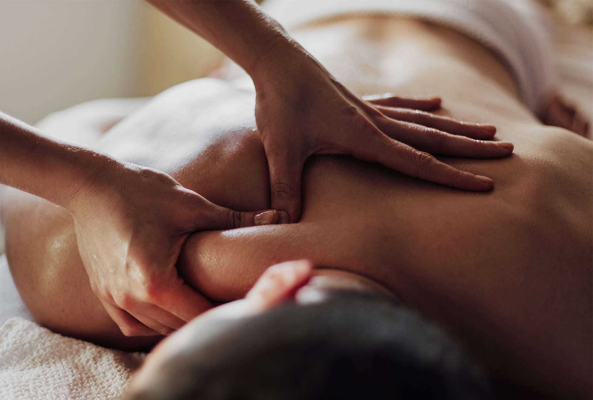 Person receiving a massage on their back, with hands applying pressure, in a relaxed setting.