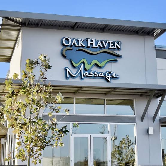 Facade of a building with a sign reading 'OAK HAVEN Massage' and a tree in front, under a clear blue sky.