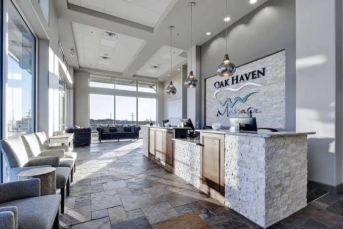 Modern hotel lobby with seating area, large windows, and a reception desk with a sign reading 'OAK HAVEN'.