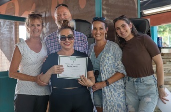 Group of five people, one holding a certificate, smiling indoors, casual clothing, bright atmosphere.