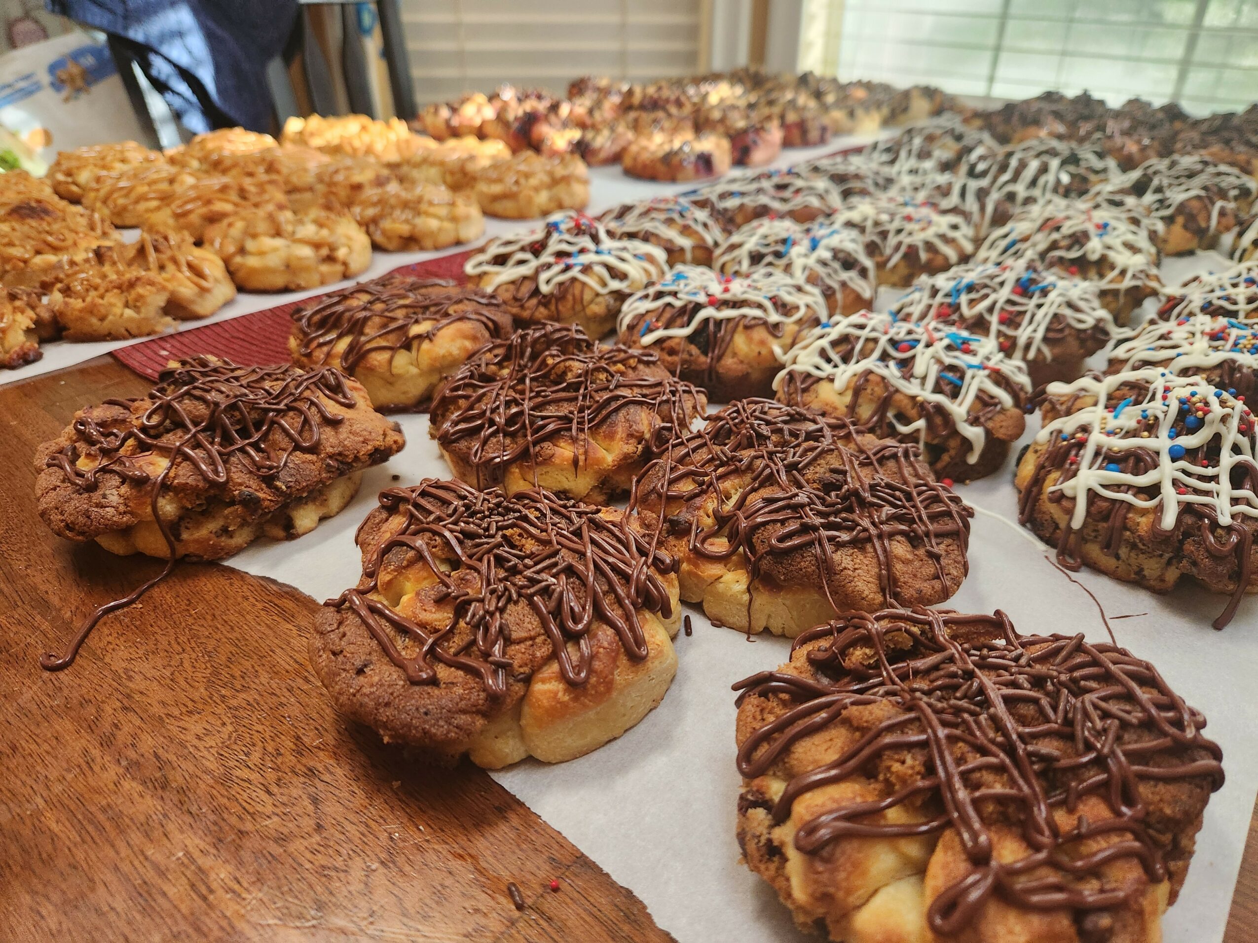 Assorted cookies and baked goods on a tray, some drizzled with chocolate and colorful icing, in a bakery setting.