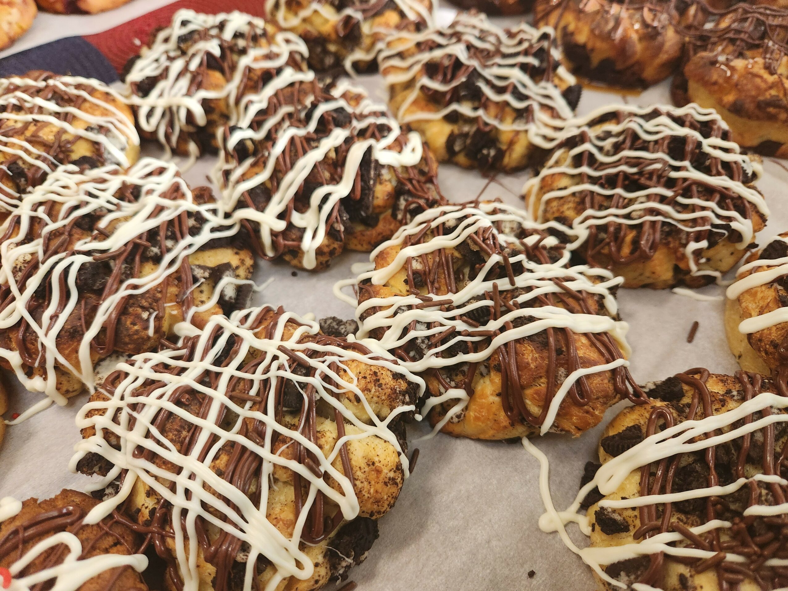 Assorted cookies topped with chocolate and drizzled with white icing, arranged on parchment paper.