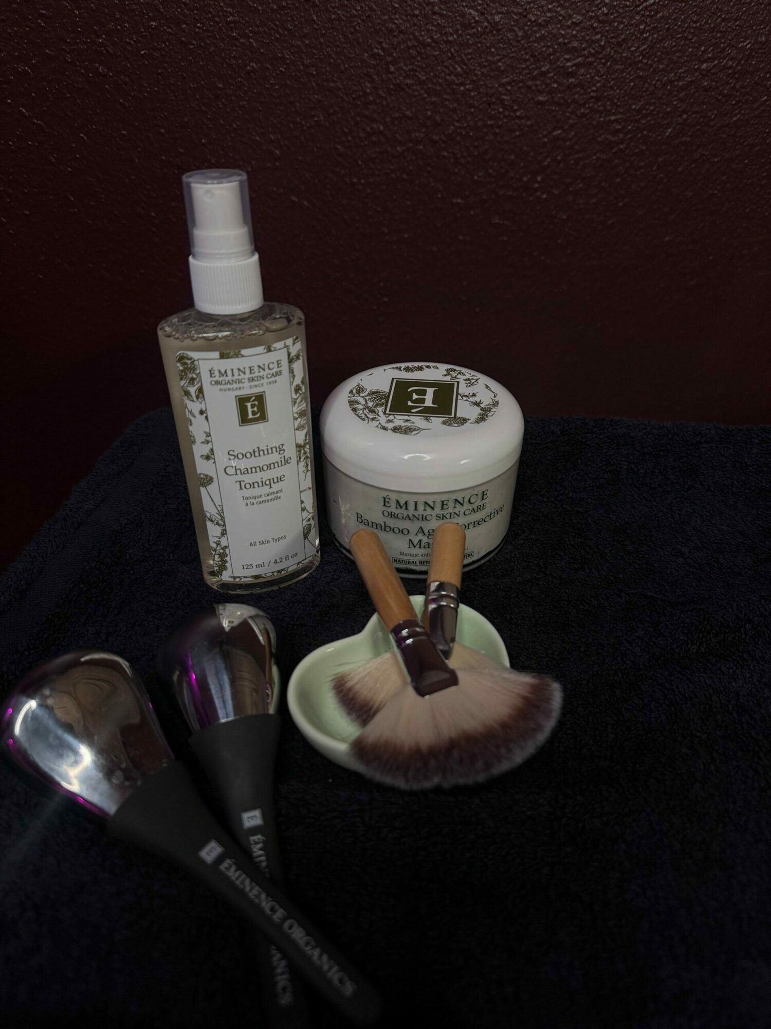Cosmetic products and brushes on a dark surface, with a dark background.